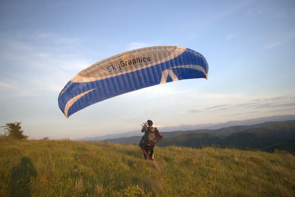 Pilot zieht am Startplatz einen blauen Gleitschirm mit SkyGraphics-Logo auf