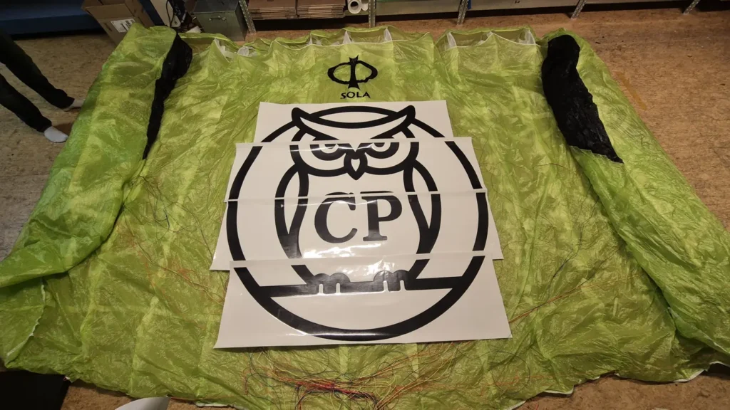 Großes Logo wird in der Werkstatt auf einem ausgelegten Gleitschirm montiert