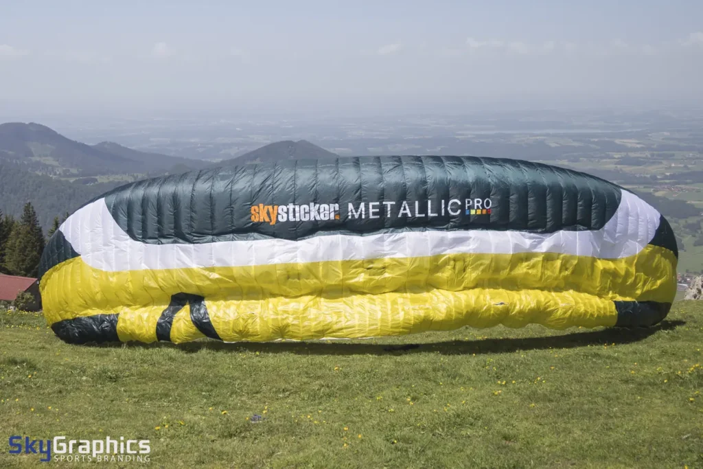 Paraglider on the ground with white skysticker METALLIC PRO lettering on dark cloth